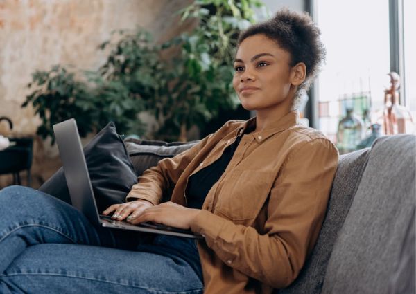 Image of a woman sitting on a couch working casually on her laptop