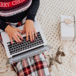 Woman sitting on the floor working on her laptop wearing a red, blue and white Christmas jumper