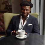 Image of an business man wearing a grey suit and white shirt drinking coffee in a cafe while using his phone